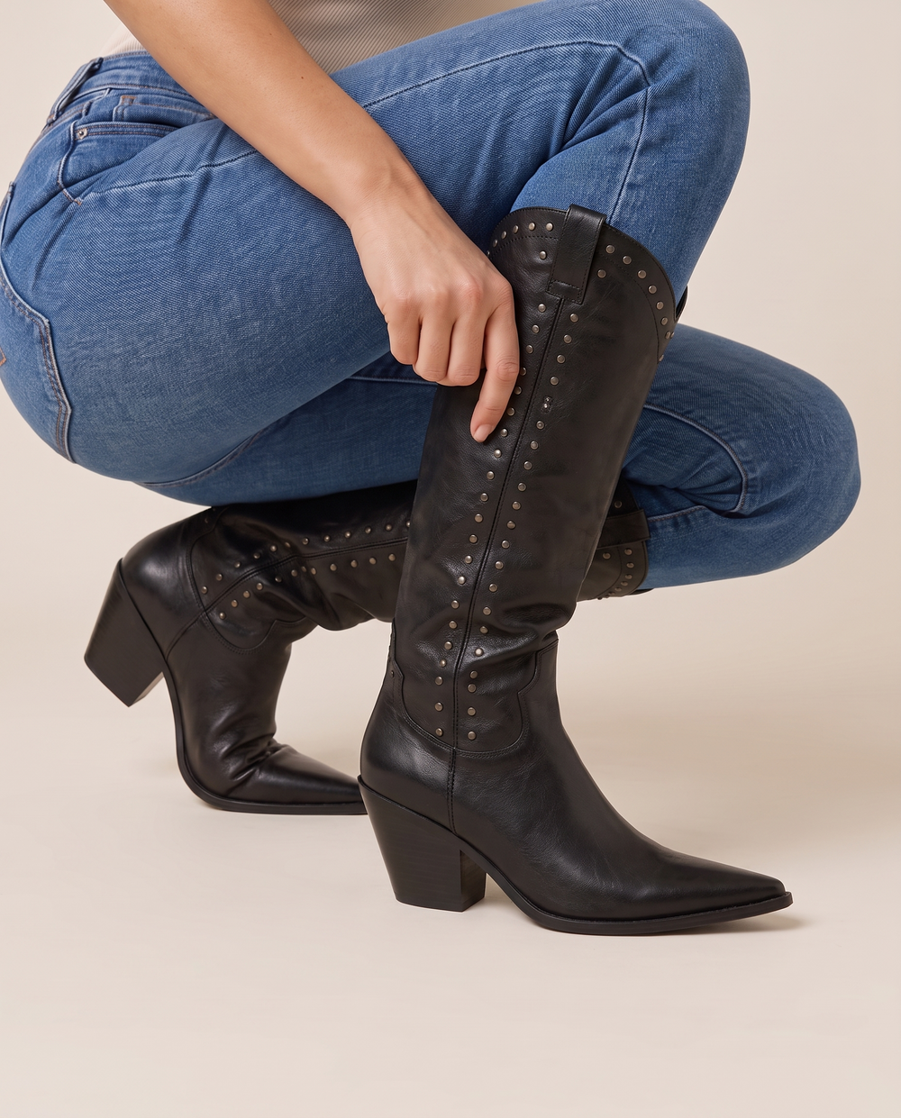 Women's Knee-High Cowboy Boots with Rivet Detail — pulling on the boot with jeans
