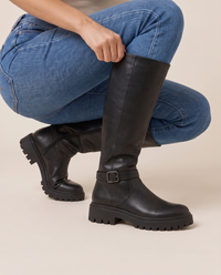 Knee-High Boots with Buckle Strap and Lug Sole — pulling on the boot with jeans