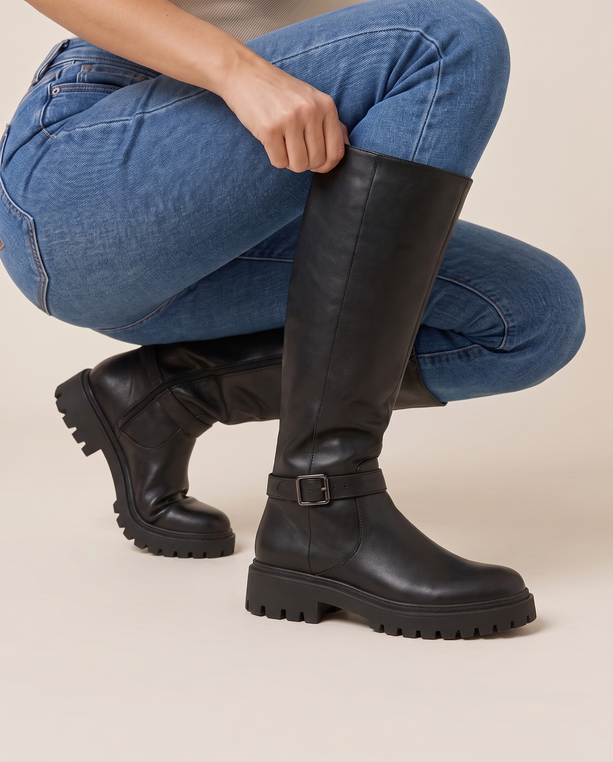 Knee-High Boots with Buckle Strap and Lug Sole — pulling on the boot with jeans
