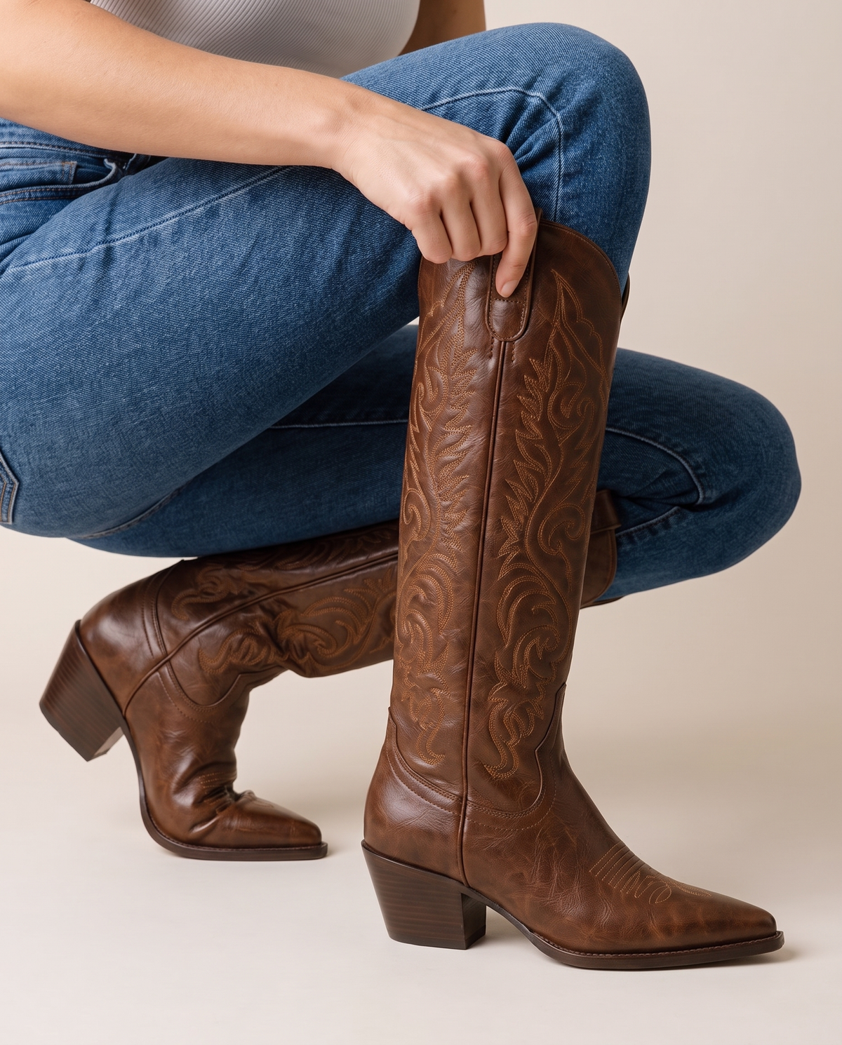 Knee-High Western Boots with Floral Embroidery — pulling on the boot with jeans