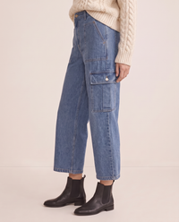 Relaxed cropped cargo jeans in blue, side view from the waist down with a cream cable-knit sweater