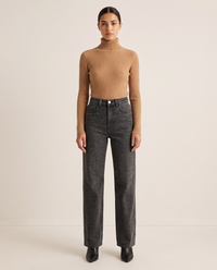 Woman wearing black leopard print straight-leg jeans with a camel turtleneck and black ankle boots, studio front view