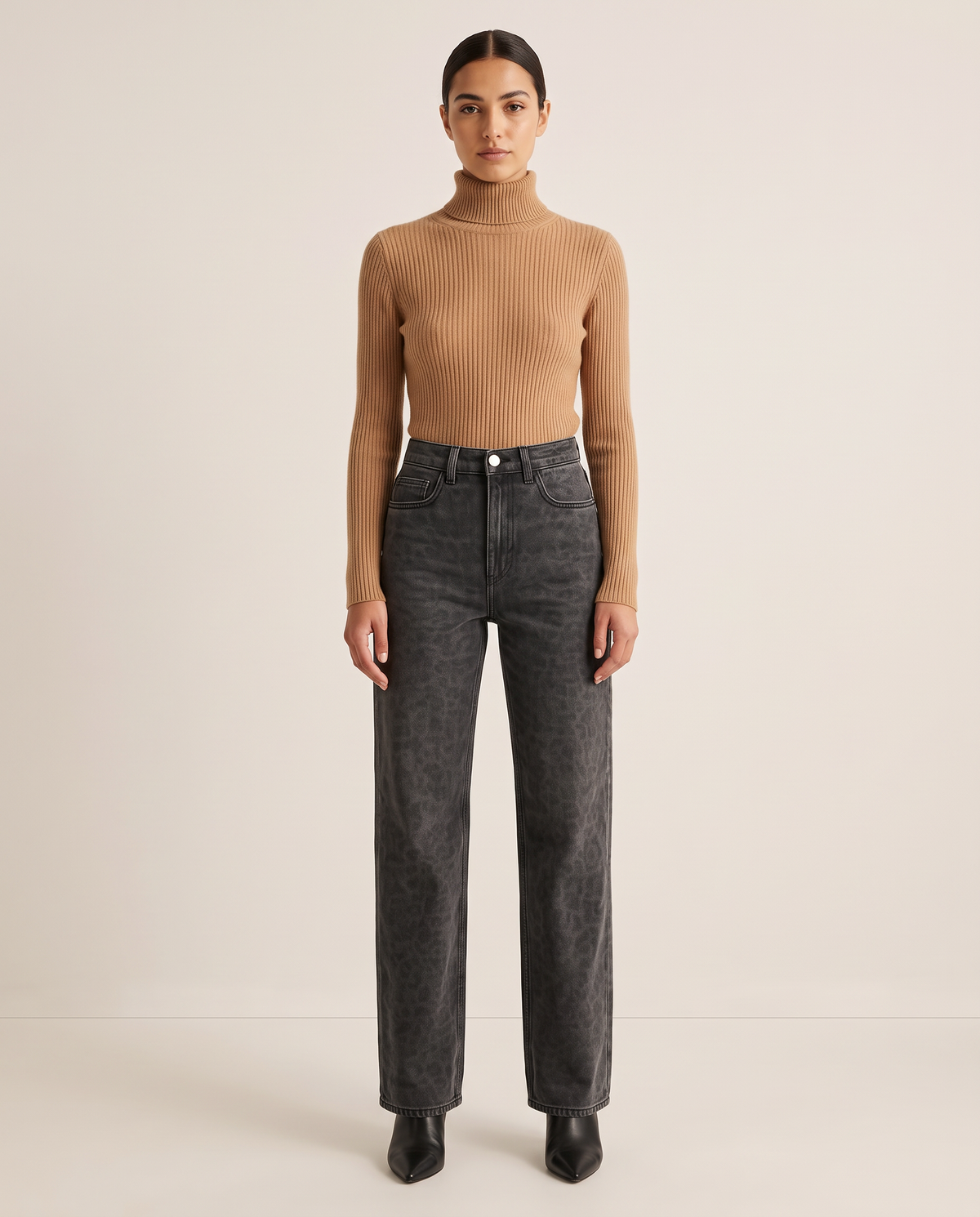 Woman wearing black leopard print straight-leg jeans with a camel turtleneck and black ankle boots, studio front view