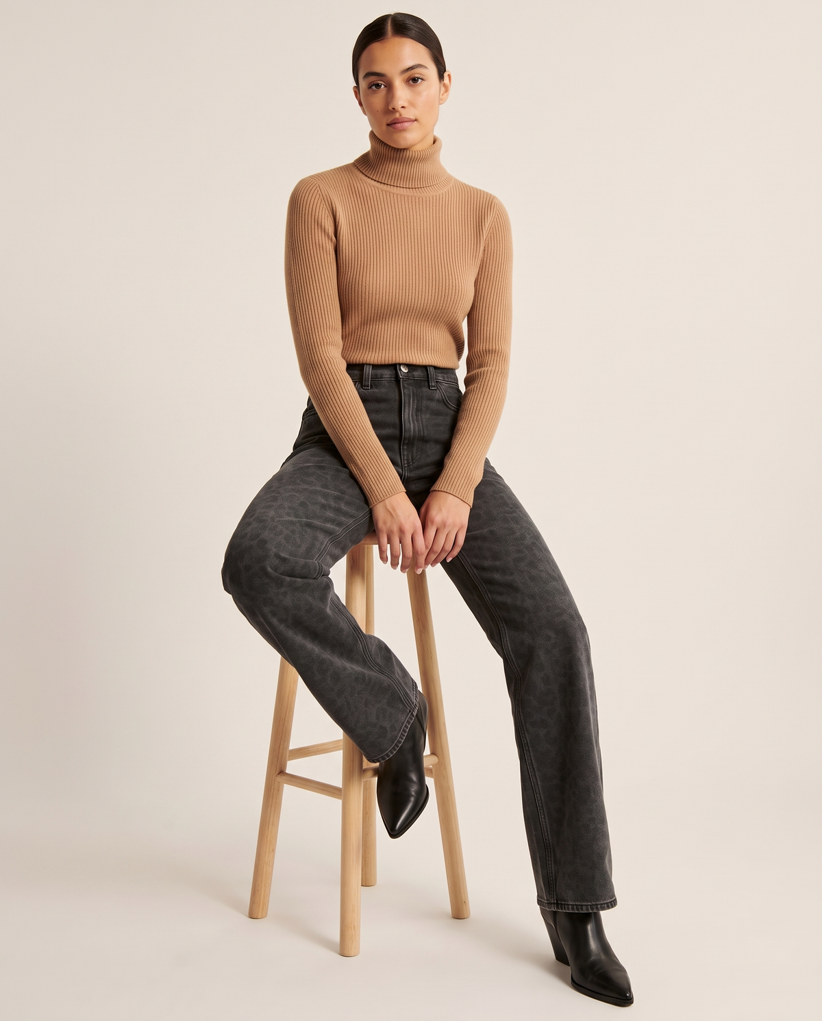 Black leopard print straight-leg jeans, seated on a wooden stool