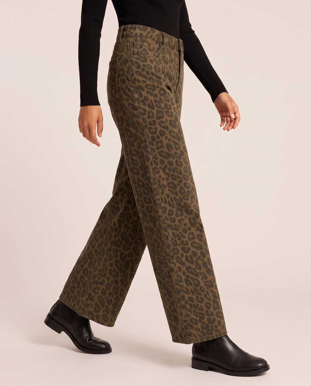Leopard print wide-leg trousers, waist-down three-quarter view mid-step with a black turtleneck and Chelsea boots