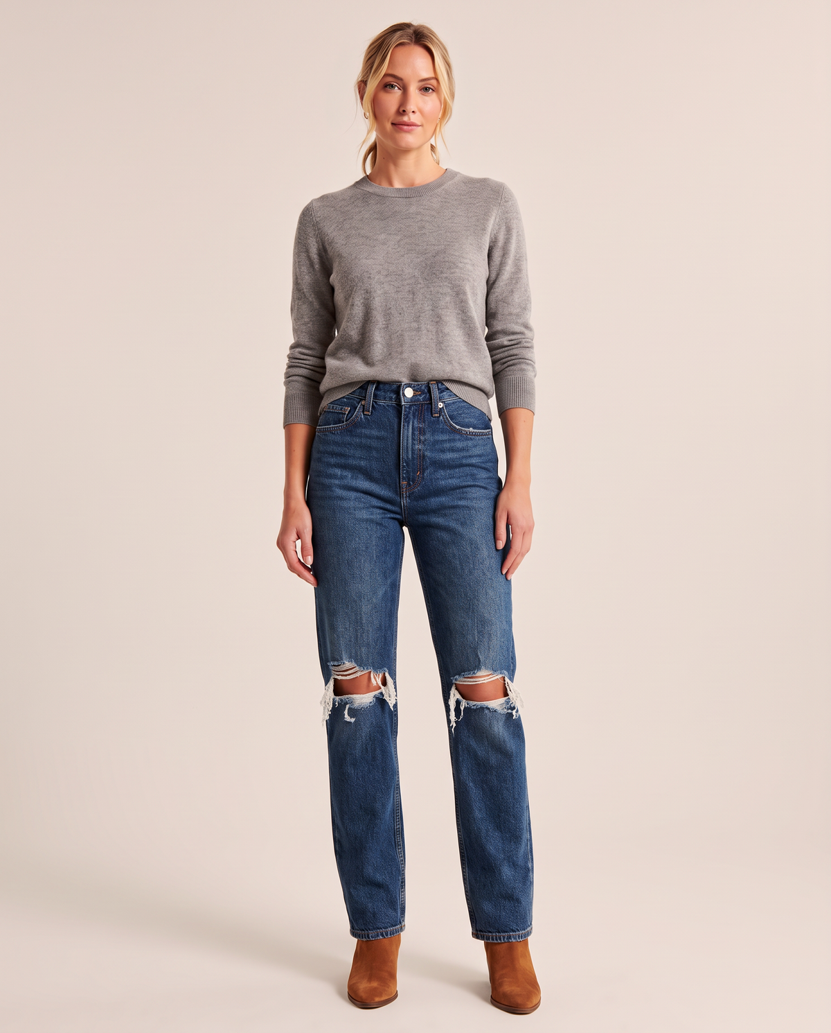 Dark blue high-waisted straight jeans with ripped knees, grey merino sweater and cognac ankle boots, studio front