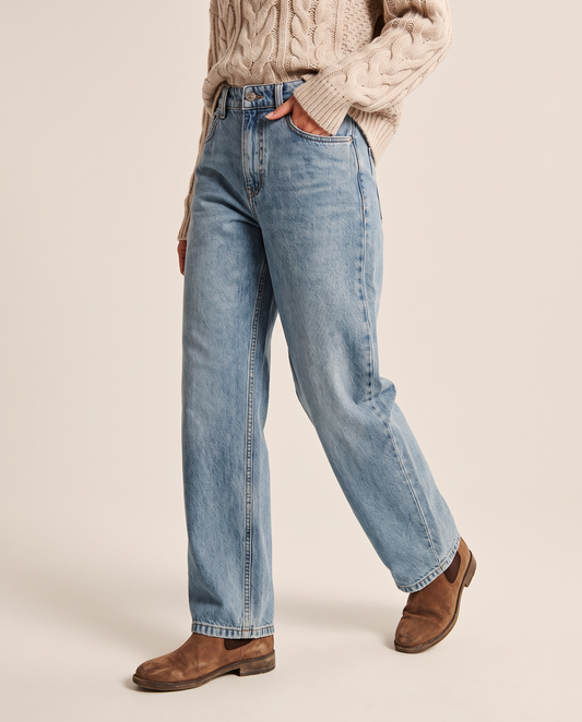 Baggy light wash jeans, waist-down three-quarter view walking with a hand in the front pocket, oatmeal cable-knit sweater and brown Chelsea boots