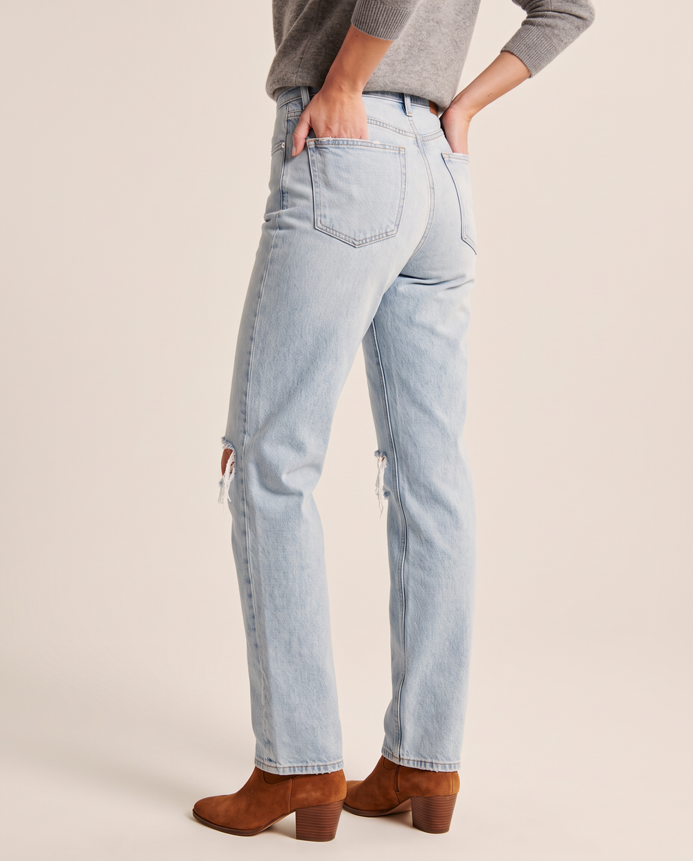 Light blue ripped straight jeans, waist-down three-quarter back view with hands in back pockets and cognac ankle boots