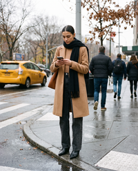 Woman in a camel coat and black leopard print jeans checking directions at a Manhattan crosswalk