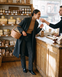 Woman in a charcoal wool coat and black leopard print jeans tasting cheese at a Brooklyn cheese shop