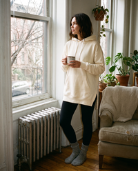 Oversized Hoodie Dress — cream, worn at home in a Brooklyn apartment with coffee