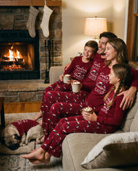 Family in matching red hockey Christmas pajamas with hot cocoa by the fireplace on Christmas Eve