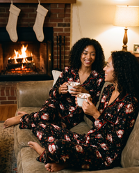 Women's Christmas Pajamas, Santa Claus Print Button-Up PJ Set — sisters in matching black pajamas with hot cocoa by the fireplace on Christmas Eve
