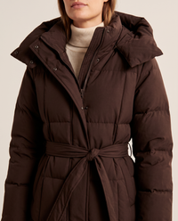 Women's Long Belted Puffer Coat — close-up of the oversized hood, zip and snap placket, quilting and tie belt