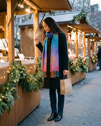 Women's Cashmere Blend Wrap Scarf in Blue — worn over a black coat at an outdoor holiday market